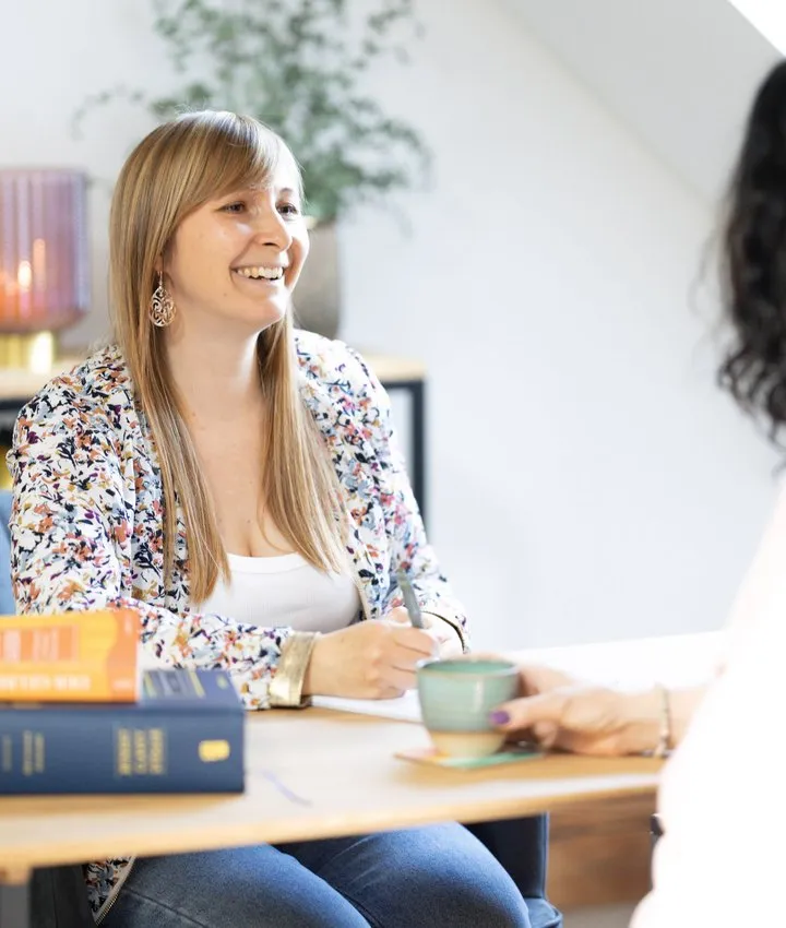 Tamara Frühwirth sitzt lachend bei einer Beratung am Tisch, neben ihr liegen Bücher